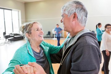 A smiling man and woman dance together in a dance class