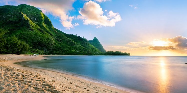 Green mountains lead down to a sandy beach in Kauai, Hawaii