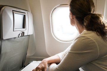 Woman sitting in a plane leans on her tray table and looks out the window