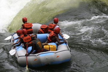 7 people in a rubber raft wearing helmets and life jackets about to go over large rapids