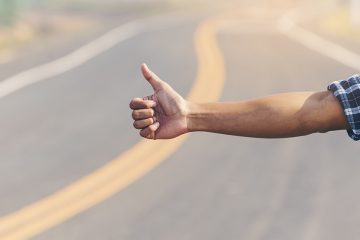 An outstretched arm giving the thumbs up on the side of a road.