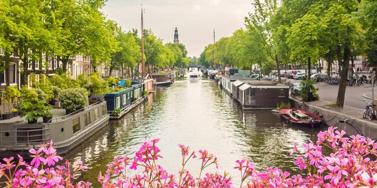 A canal in the Netherlands includes boat homes and a boat tours of the city of Amsterdam