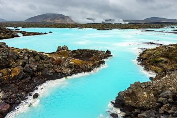 A geothermal spa with vibrant aquamarine colors is surrounded by natural rock formations