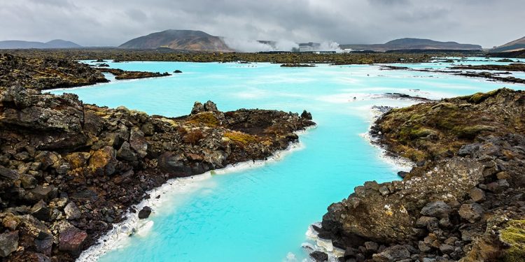 A geothermal spa with vibrant aquamarine colors is surrounded by natural rock formations