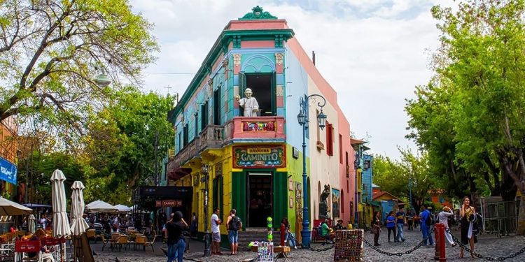 A multi-colored building with a sliver statue on the balcony with tourists taking photos