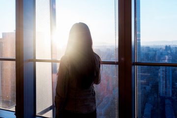 A woman is watching the sunrise from her condominium windows