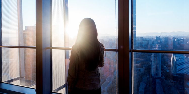 A woman is watching the sunrise from her condominium windows