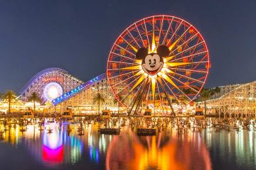 A giant lit ferris wheel includes a giant picture of Mickey Mouse's face in the middle, with numerous roller coasters in the background
