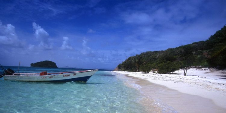 A boat is placed along the sandbars of a quiet beach with white sand