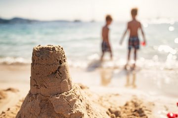 A handmade sand castle is in focus with two young children in the background