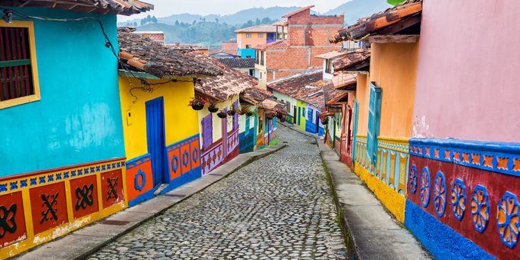 A cobblestone road contains numerous houses are painted with colorful vibrant colors of yellows, blues, pinks, reds, purples, and greens on either side