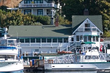 Two large boats are docked by a boating white house with a green roof