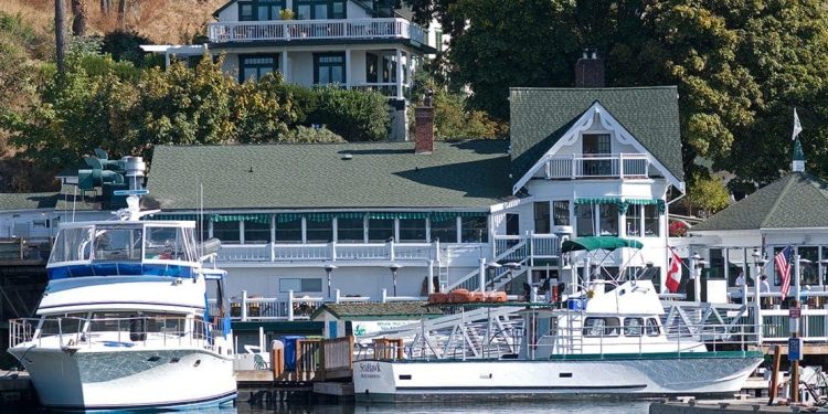 Two large boats are docked by a boating white house with a green roof