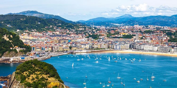 A Spanish coastal city of colorful buildings curves around the beautiful blue bay of water and white sand