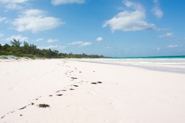 Footprints are imprinted on the beach's white sand with emerald color ocean water to the right