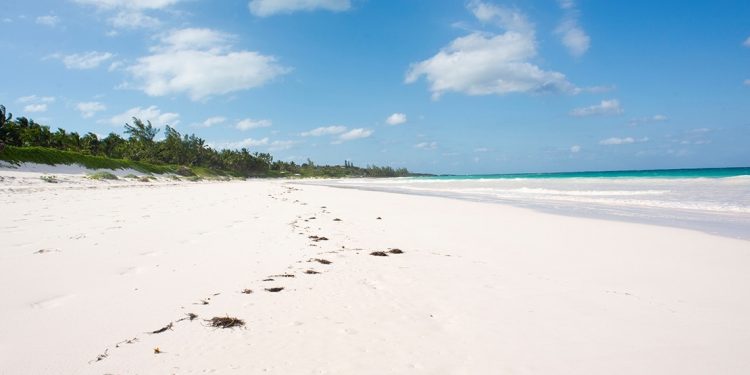 Footprints are imprinted on the beach's white sand with emerald color ocean water to the right