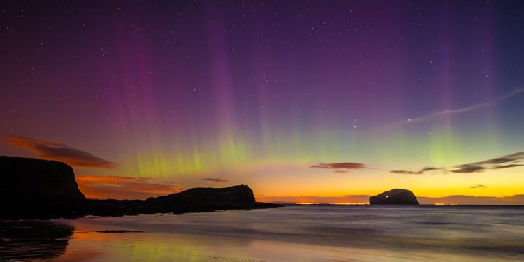 The Northern Lights begin their appearance as the sun sets over a Scottish city