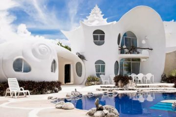 A white seashell inspired home comes is two stories high with an outdoor patio and swimming pool