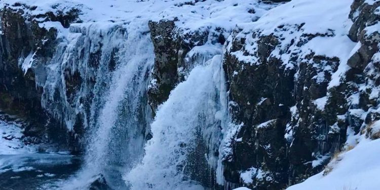 An almost frozen waterfall with icicles and snow continues to spout water