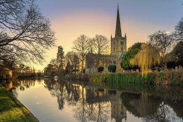 An old English church is located by a calm, reflective river