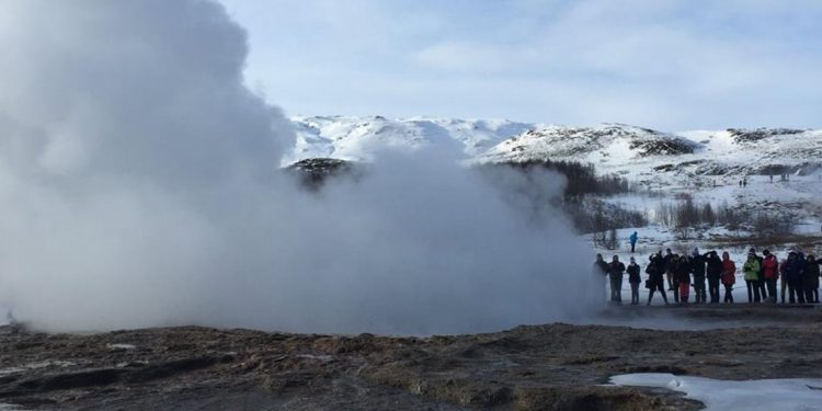 Tourists are photographing a geyser that recently ejected a column of hot water and steam