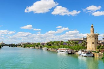 Wide river with tour boats docked along concrete ledge on right hand side.