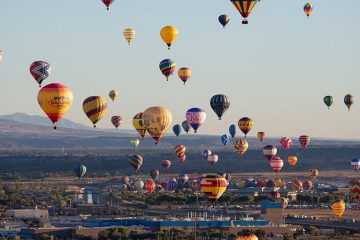 Numerous colorful hot air balloons fly above a city