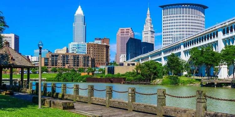 A photo of downtown Cleveland featuring a river and a city landscape in the background during a sunny clear day