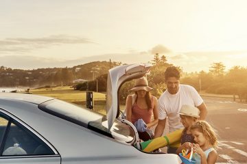 A family of four is packing their luggage in the car's back trunk