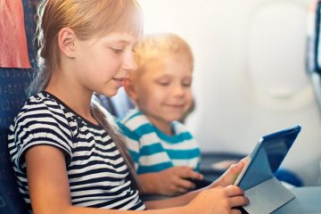 Two kids playing with a tablet in their airplane seats