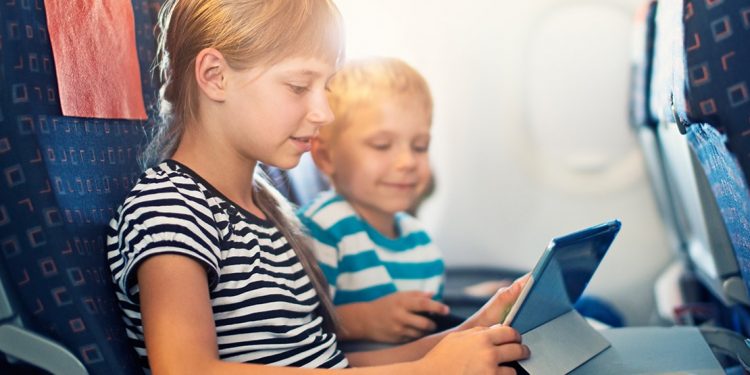 Two kids playing with a tablet in their airplane seats