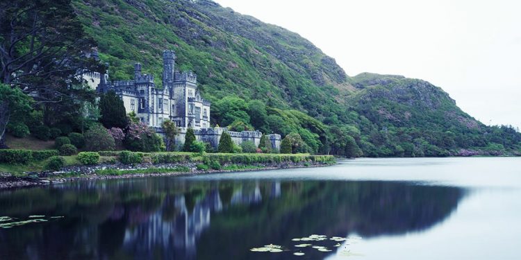 A beautiful abbey sits alongside a beautiful glistening lake on a cloudy day