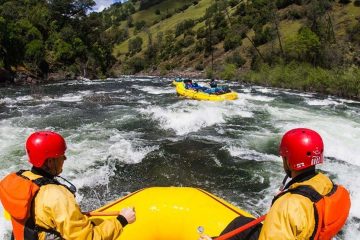 Two individuals watch a group of people white water rafting