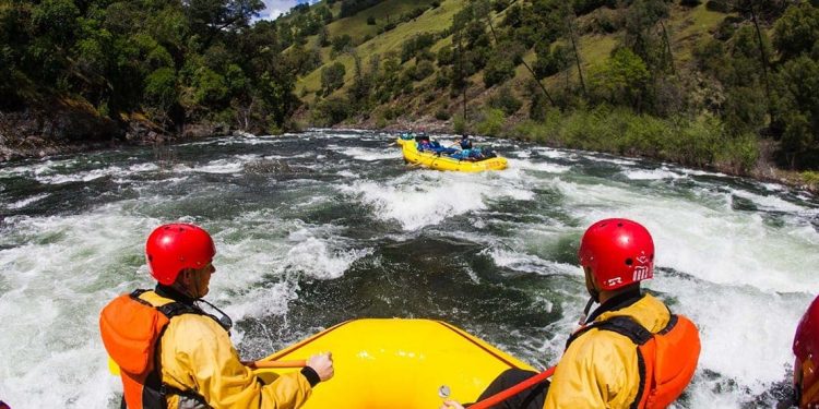Two individuals watch a group of people white water rafting