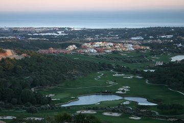 The Spanish country side includes a large golf course with large bodies of water and a small colorful town in the distance