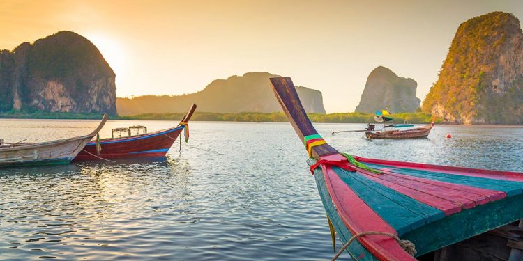 Three boats are drifting along the stunning Thailand waters during the sunset