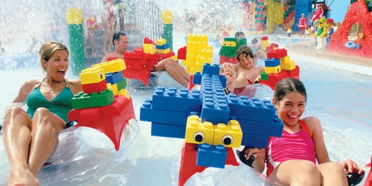 A family is floating down the water park ride with oversized lego pieces on their inflatable tube