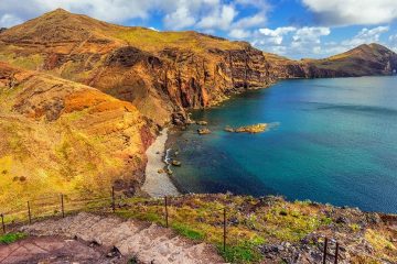 Yellowish brown cliffs next to deep blue sea. Stone steps winding down along the cliff side.