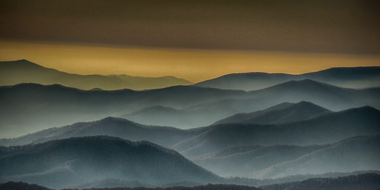 Silhouetted hills overlapping in layers with yellowish sky in the distance.