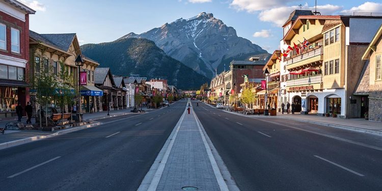Looking down the middle of the street in Banff. Quaint stores on either side and mountain rising up at end of the road.
