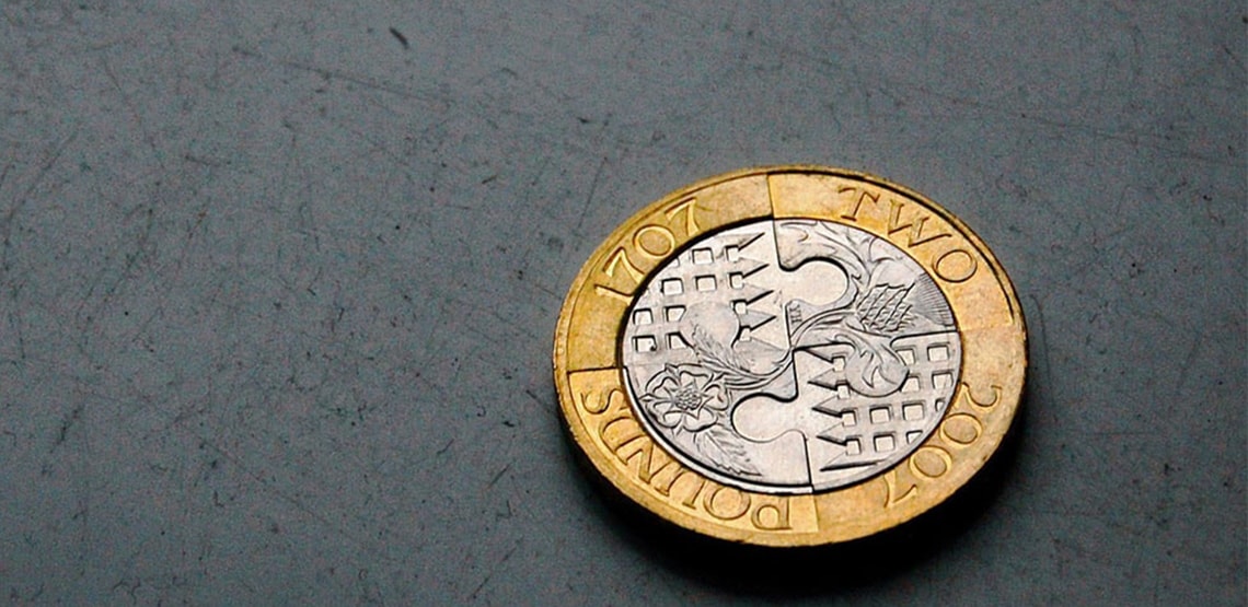 A close-up of the British pound: round coin with gold edge and silver middle.