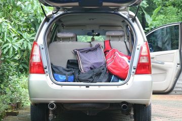 Hatchback trunk open with bags piled in trunk and passenger side door open.