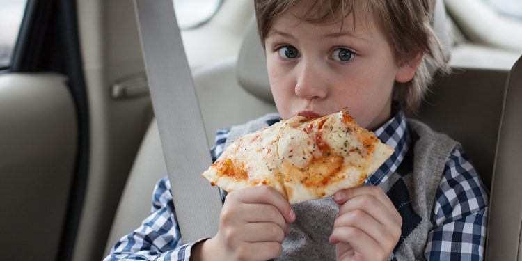 Little boy eating slice of pizza in car.