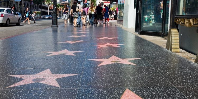 Pink stars inset in the grey sidewalk with names of famous actors. People walking further down the sidewalk.