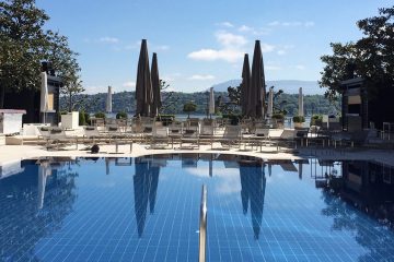 Pool with closed brown beach umbrellas and grey lounge chairs around on the deck.