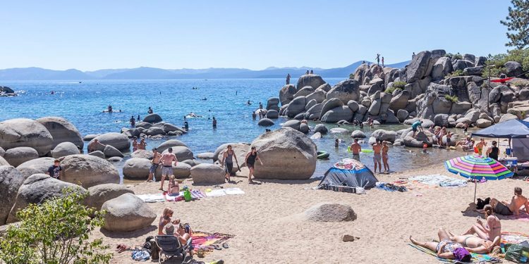 People sunbathing on the beach with giant boulders in and around the water.
