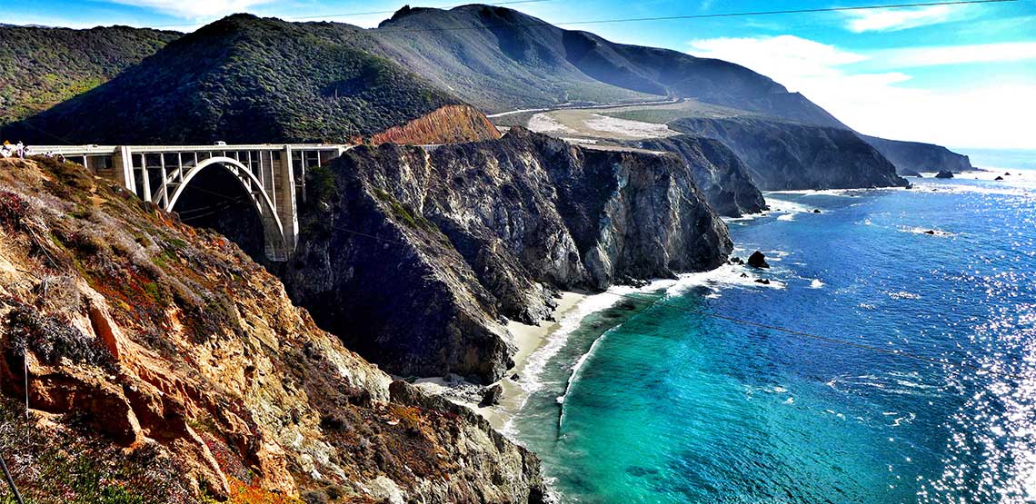 Bridge leading from one cliff face to another with ocean down below.
