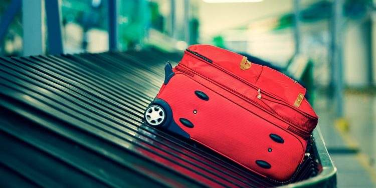 Red suitcase sitting on a conveyor belt at airport.