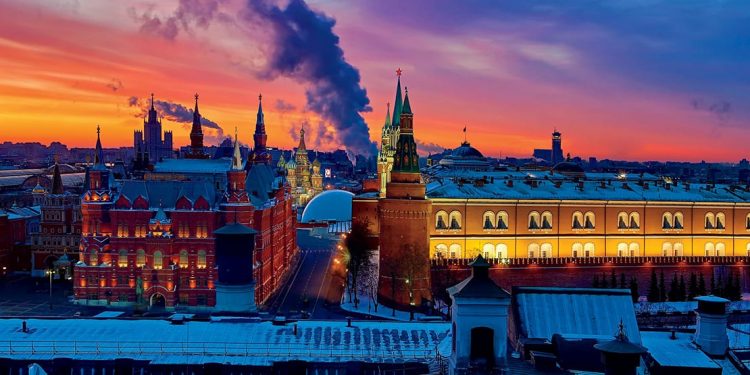 Russian-inspired building with towers and spires, smokestacks spewing smoke in the background against a red sky.