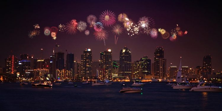 Water and boats in the foreground with skyscrapers lit up in the background and fireworks over top.